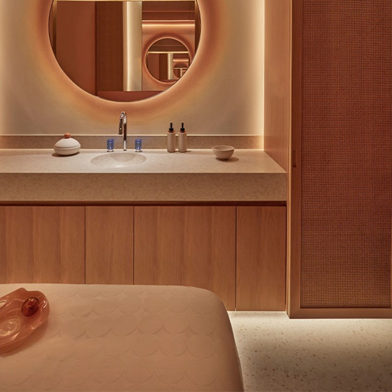 Serene treatment room with a massage bed and softly lit round mirror above a light wood vanity