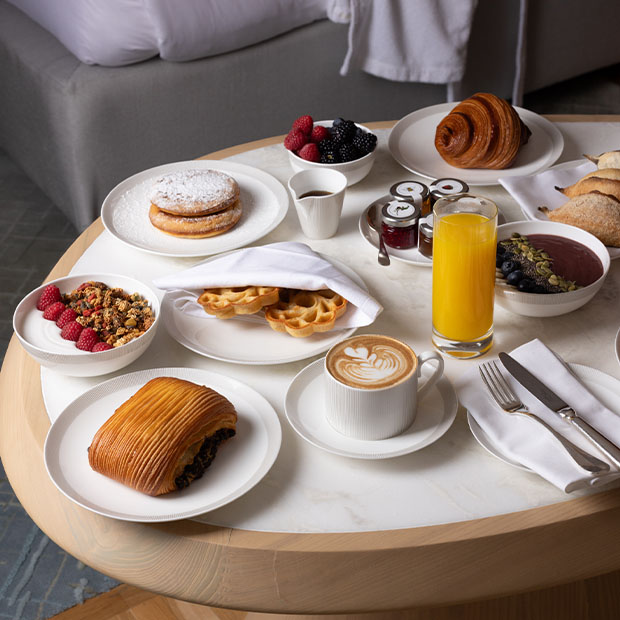 Breakfast table with pastries, waffles, berries, granola, coffee, juice and preserves arranged neatly.