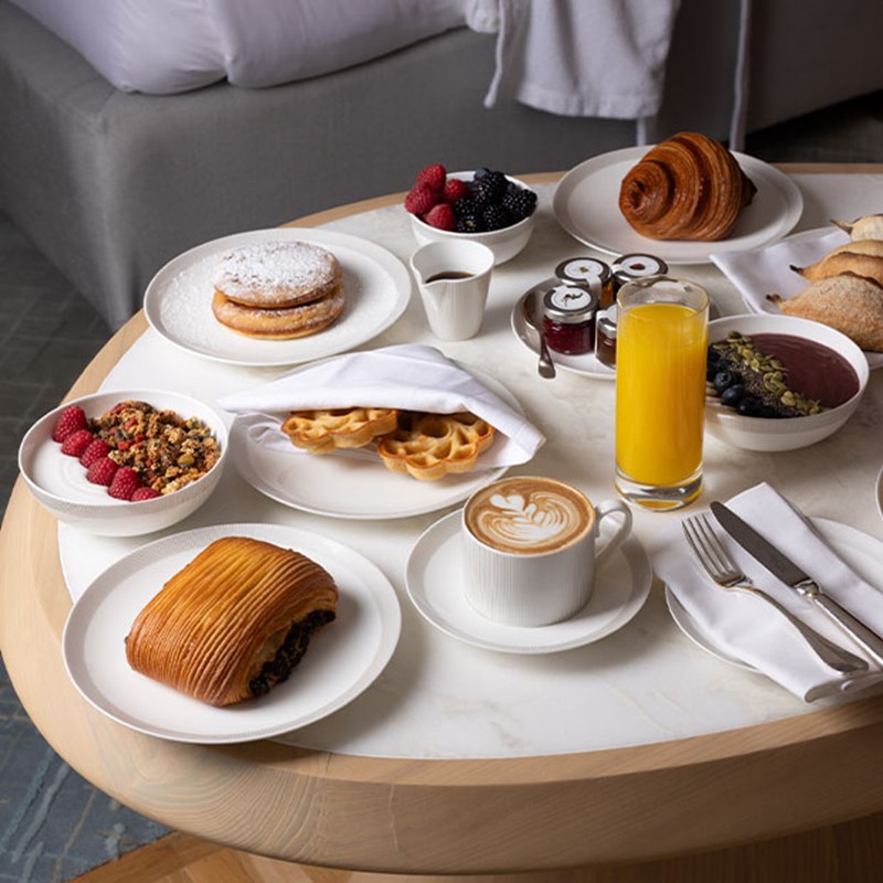 Breakfast table with pastries, waffles, berries, granola, coffee, juice and preserves arranged neatly.