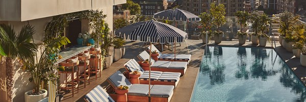 Rooftop poolside lounge at The Berkeley with striped sun loungers, parasols, and fruit bowls, overlooking a city skyline under clear skies.