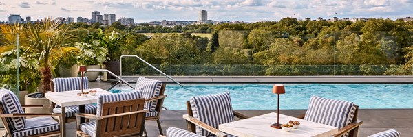 The Berkeley rooftop pool, with small square marble tables with blue & white striped chairs …